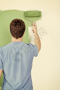 英俊的青年男子用彩色漆白白墙职业工匠蓝色滚筒工作房间装修工人画家乐趣图片