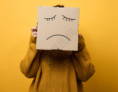 一个身穿棕色毛衣 头上戴着盒子的女人站在黄色背景上 悲伤的鬼脸 压力和抑郁的概念 精神健康图片