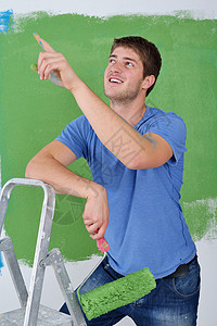 英俊的青年男子用彩色漆白白墙维修画家工匠蓝色工人男性滚筒房间职业工具图片