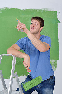 英俊的青年男子用彩色漆白白墙画家职业男性工作微笑工匠蓝色装修刷子房子图片