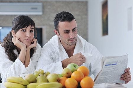 早餐时在厨房看报纸快乐的一对情侣女士女孩成人杯子橙子男性乐趣黑发食物阅读背景
