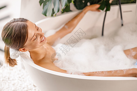 可爱的年轻女子在家浴缸休息时 享受洗澡泡泡泡水图片
