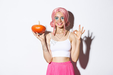 快乐女孩的肖像 庆祝万圣节 展示小南瓜和好姿态 穿着可爱的粉红色假发图片
