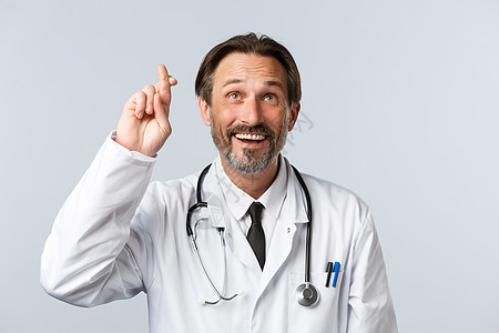 Covid19 预防病毒 医护人员和疫苗接种概念 乐观有希望的医生穿白大褂的特写 交叉手指祝你好运 抬头微笑 许愿急诊室诊所实验图片