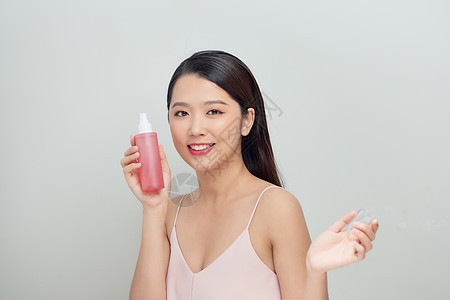 一名年轻女子拿着粉红瓶子 用白底润色涂在白色背景上肖像护理奶油女士润肤化妆品保湿皮肤洗剂治疗图片