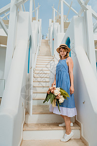 美丽的女孩带着花束走在希腊欧洲古老小镇圣托里尼岛的街道上 一个走在街道背景上的旅游女孩的画像 爱情故事暑假游客潮人旅游摄影师爱情背景图片