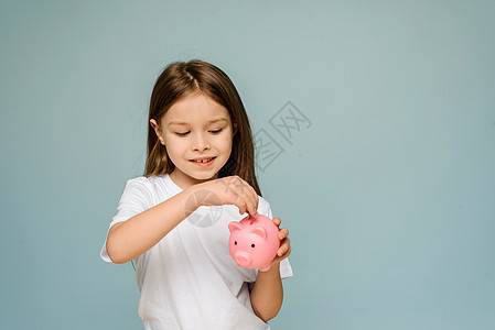 一个小女孩把硬币放进小猪银行里 教孩子个人财务和储蓄的理念 笑声货币蓝色商业投资现金快乐童年微笑女性金融图片