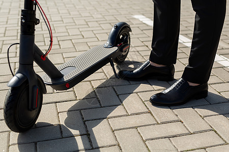 穿着商业西装和鞋贴近一个男人的脚 在一辆电动摩托车旁边技术活力自行车城市闲暇骑术潮人运动鞋青年街道图片