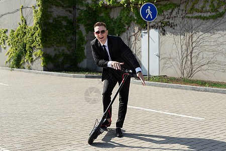 穿着商业西装的男人在一辆电动摩托车旁边笑着玩图片