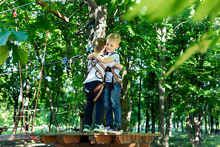 在冒险公园的两个可爱男孩 正在攀岩或在绳子路上通过障碍物 抱抱着图片