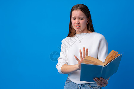年轻美女拿着书本 惊吓和惊讶 在工作室的蓝背景图片