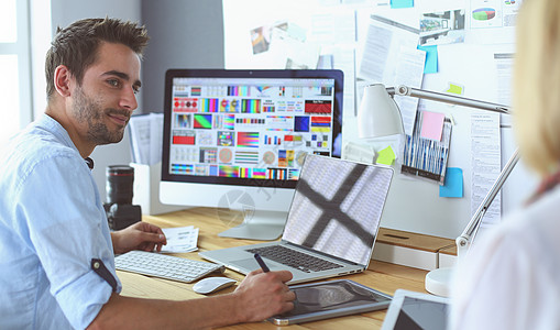 年轻设计师在网上工作时 在笔记本电脑和笔记本电脑前的图形演播室上坐着职业工作室社论商务人士报纸杂志互联网记者邮件图片