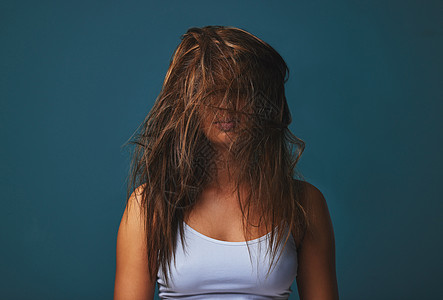都是乱七八糟的 头发 床 文字 甚至是心……工作室拍摄的一位年轻女子用头发遮住脸 在蓝色背景下摆姿势图片