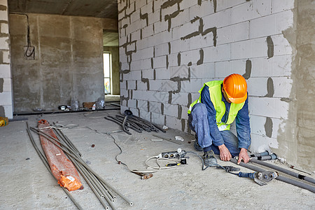 身着工作服和橙色安全帽的建筑商正在使用现代工具在正在建设的建筑中安装塑料管图片