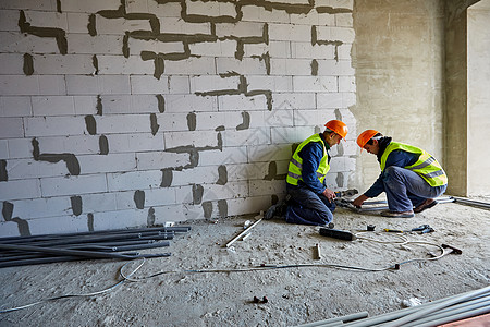 两名身着工作服 头戴安全帽的男性建筑工人正在使用现代工具在正在建设的建筑中安装塑料管图片