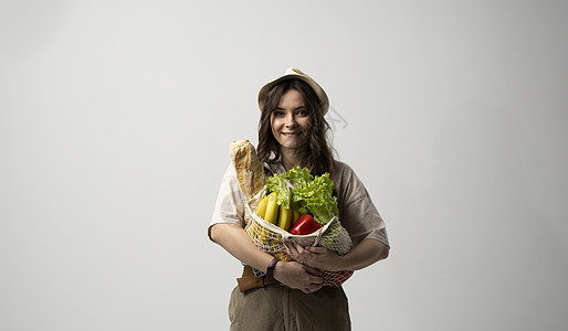 身穿米格超大T恤的生态友好型年轻女子 持有可重新使用的网棉杂货袋 用白底有机食品购物图片