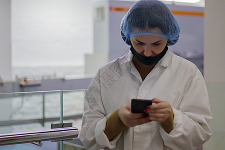 质量检查员或食品专家在现场 工业设施中身穿白大褂 头戴帽子的员工正在查看智能手机 糖果厂工人穿着白大褂图片