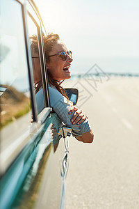 在开阔的道路上自由自在 一个迷人的女人在享受公路旅行时挂在车窗外的镜头图片