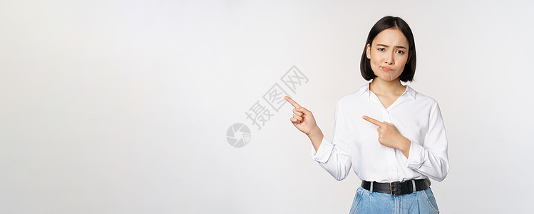 在白人背景下站立 对持怀疑态度的亚洲女性进行咆哮 指左手和抱怨 表示憎恶或不赞同的肖像女孩企业家女士技术商务快乐成人办公室员工公图片