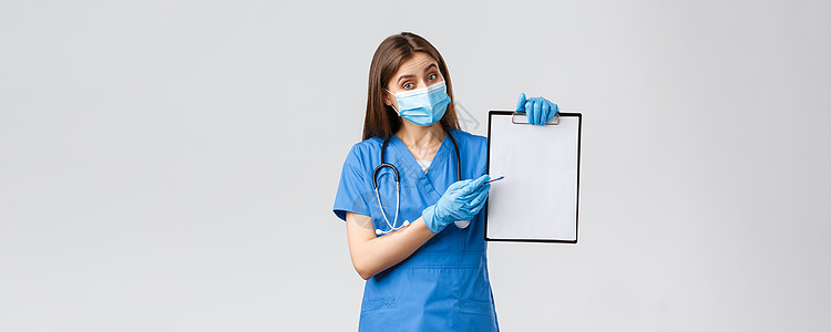 Covid19 预防病毒 健康 医护人员和检疫概念 穿着蓝色磨砂膏和医用口罩的友善女护士或医生 在剪贴板上解释信息 指着纸暴发防图片
