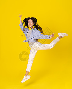 年轻快乐的女孩跳在黄色背景上 亚洲年轻女人长发苍蝇的芭蕾风格图片