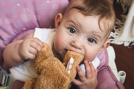 可爱的女婴玩着棕色泰迪熊 柔软玩具和咀嚼熊脚图片