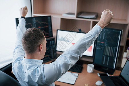 由于成功而举起手来 在办公室在线工作的人 在索引图表中挂有多个计算机屏幕图片