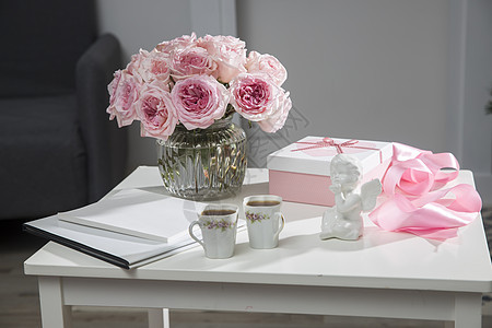 玻璃花瓶中的一束粉红色玫瑰 两个带茶的瓷杯 一个带心形礼物的白色盒子 一条缎带 一个天使雕像  咖啡桌上的情人节礼物花束纪念日花图片