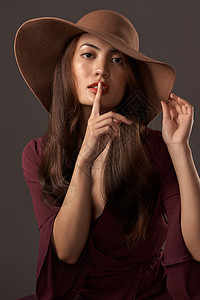 一个有魅力的年轻女人在演播室用灰色背景 用手指朝她嘴唇摆布的肖像画 照片被剪辑了图片