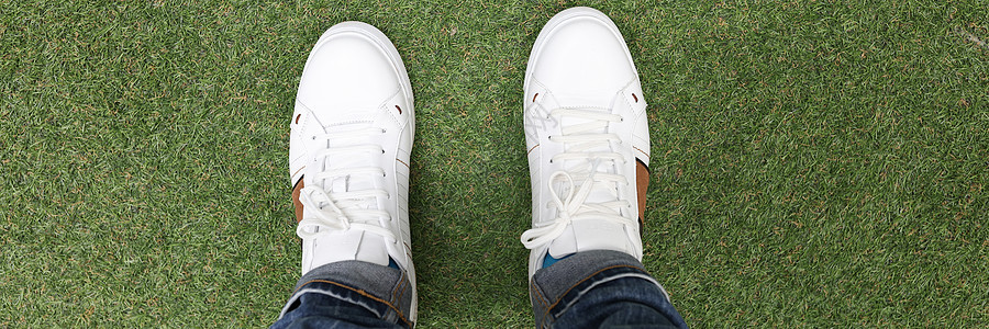 穿着白色运动鞋的男性脚站在绿色草地上图片