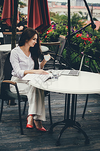 年轻的自由职业者使用笔记本电脑坐在咖啡桌旁 微笑的女人在网上工作或学习 同时使用笔记本工人写作互联网职业网络人士女士咖啡技术女孩图片