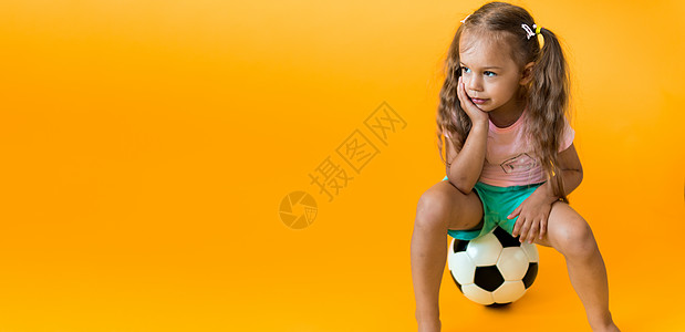 带着经典黑白足球的正宗可爱微笑学龄前小女孩看着黄色背景的相机 孩子们穿着 T 恤和短裤踢足球 运动 冠军 团队理念女士竞赛比赛母图片