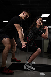 男教练员在健身房训练一名身着环管系统西装的女孩 在积极培训期间刺激了精神错乱症锻炼肌肉药品生活工具技术建筑快乐刺激器女士图片