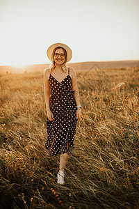 女人穿着洋装 戴着波尔卡圆点戴帽子 穿过草地女性太阳美丽女士女孩日落裙子阳光喜悦微笑图片