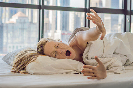 女人早上在市中心的一间公寓里醒来 可以看到摩天大楼 生活在大城市概念的喧嚣中 睡眠不足城市商务情感办公室建筑超载大人枕头唤醒女孩背景图片