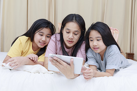 幸福的亚洲家庭在卧室的床上享受和放松 母亲和女儿喜欢在床上一起使用平板电脑 家庭观念活动学习技术药片母女小姑娘笔记本房子女士父母图片