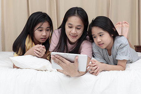 幸福的亚洲家庭在卧室的床上享受和放松 母亲和女儿喜欢在床上一起使用平板电脑 家庭观念药片互联网技术财产孩子们成人父母微笑学习女性图片