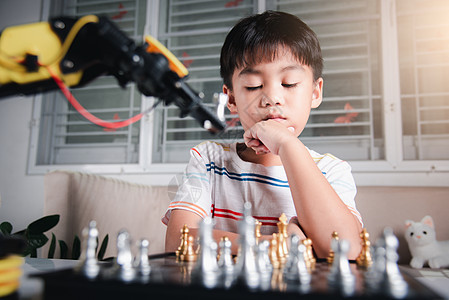 亚洲小男孩思考和等待机器人臂象棋游戏的亚洲男孩男生智力助手学习电子产品机械作坊童年工程学校图片