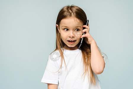 天啊 在演播室的蓝色背景下 震惊的小女生拿着智能手机到她的耳朵 一个小女孩正在打电话 很惊讶 复制空间图片
