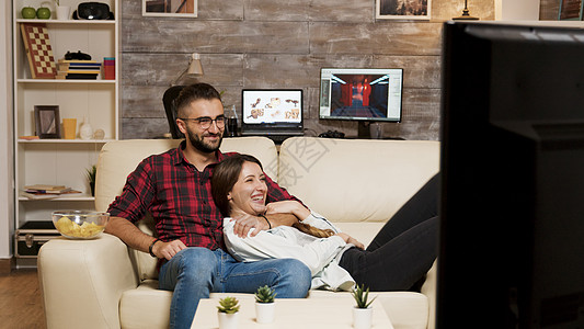 有魅力的年轻夫妇在沙发上放松 一边看电影电视节目长椅程序男人夫妻恋人专注电影房子电视图片