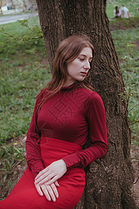 一个穿红衣服的女孩 躺在春林的一棵树上金发头发帽子公园眼睛金发女郎毛毡植物群裙子长发图片