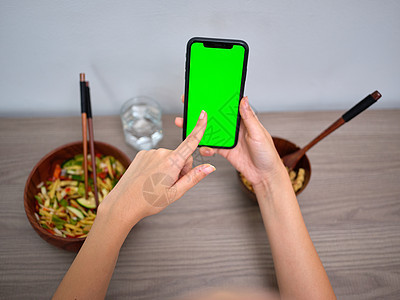 女性食用东方食物 同时指着手机的绿色屏风点图片