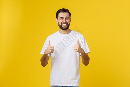 年轻快乐的男子与拇指举起标志 在空闲中孤立在黄色背景上微笑成人男人成功喜悦白色衬衫工作室男性胡须图片