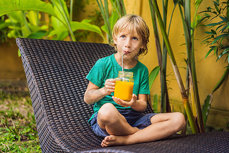 男孩在泳池背景上用钢稻子 在玻璃泥瓦罐中喝芒果的多汁滑雪 吃着美味的冰淇淋 健康的生活概念 复制空间果汁味道水果浆果异国饮料孩子图片