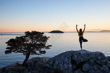 年轻女子在青春的夕阳下 在岩石岛做瑜伽女孩日落娱乐海洋岩石运动风景场景女士天空图片