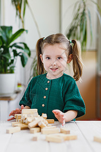 身着绿色衣服和破碎的木制Jennga塔台在桌子上微笑的 又可爱又傻又可爱的孩子图片