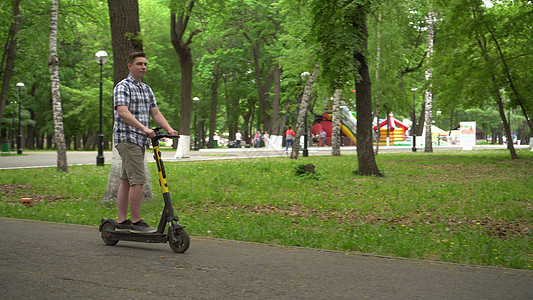 一名穿衬衫和短裤的欧洲青年骑着电动摩托车在公园里行驶男性驾驶运输街道电话男人工具生态技术游乐图片