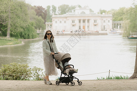 一位母亲在宫殿内的婴儿车里冒着孩子的面容日光公园童年晴天女孩休闲新生女士阳光花朵图片