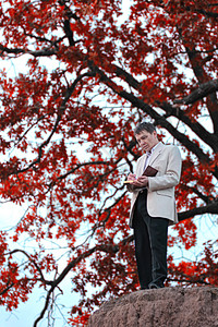 一个手拿着一本书的人 站在树底的树上 有红叶子图片