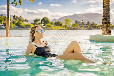 身心放松豪华度假村游泳池 美丽的女游客在暑假度假时放松身心 享受海洋背景的日光浴泳装的比基尼泳装女孩温泉热带女士皮肤假期游泳横幅全景太阳背景
